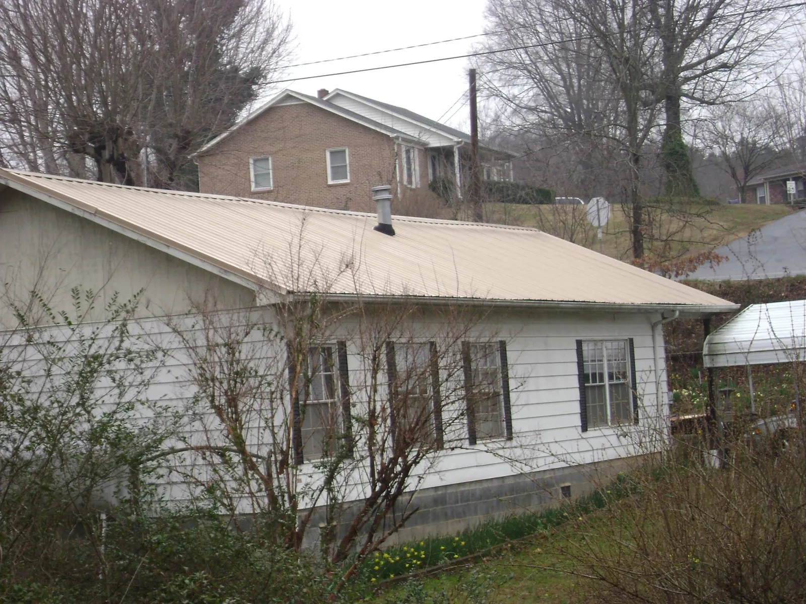 Tan metal roof on a white sided house set into a hillside — Commercial Roofing by Roofing Brothers in Spencer